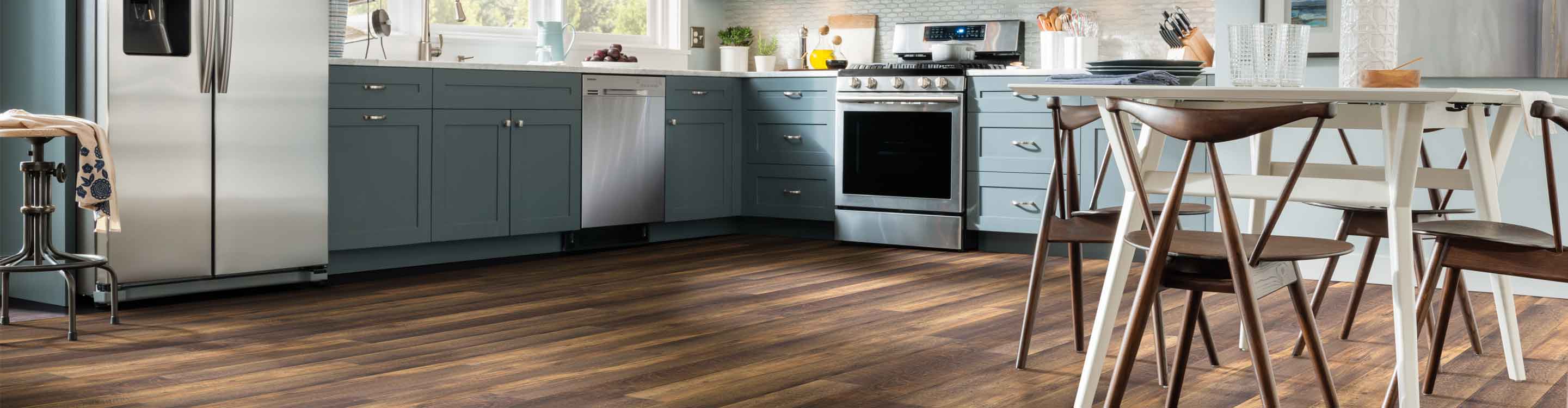 dark hued wood look vinyl flooring in modern kitchen with blue cabinets, white table, and wood chairs